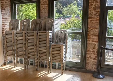 Stacks of plastic chairs by the window in a bright indoor space with sunlig.. Stock Photos