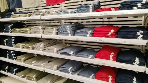 Stacks of T-shirts in different colors are on the shelves of a clothing store Видео 220445583
