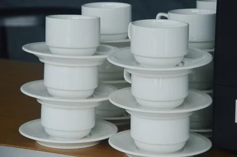 Stacks of white ceramic dishes - cups and saucers stand on a wooden table. Ki Stock Photos