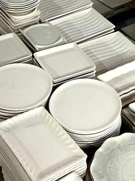 Stacks of white ceramic plates and dishes are neatly arranged at a pottery st Stock Photos