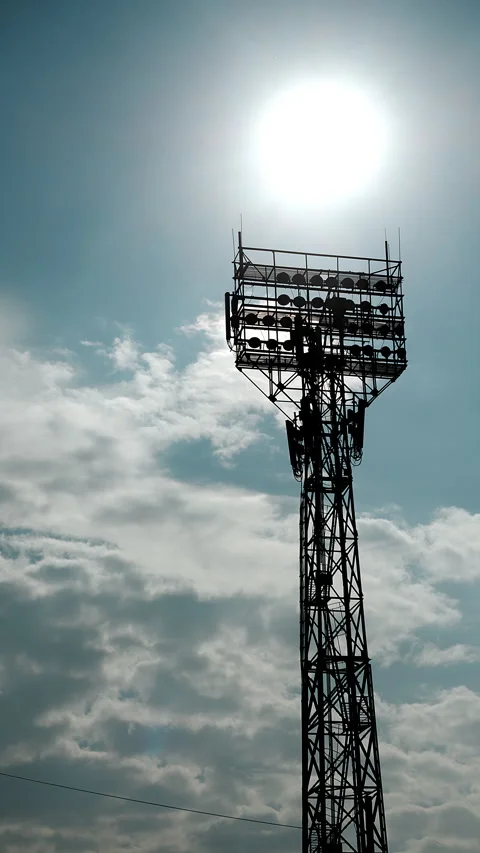 Stadium Floodlight Tower Against Bright Sun and Cloudy Sky Stock Footage 345560234