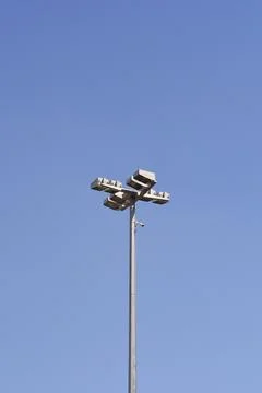 Stadium floodlight tower with security camera against blue sky Стоковые фото