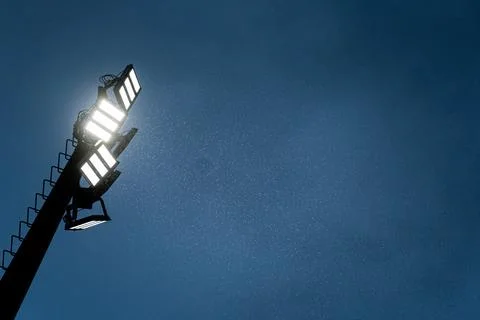 Stadium lights illuminating falling rain against blue sky Stock Photos