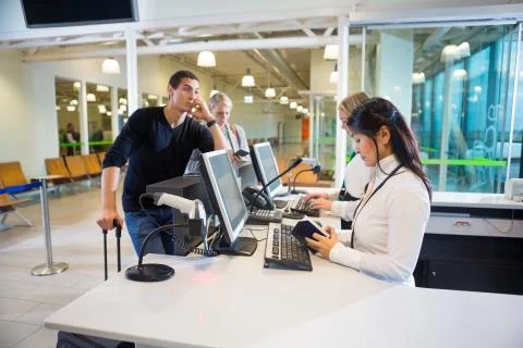 Staff Examining Passport While Passengers Waiting In Airport Stock Photos