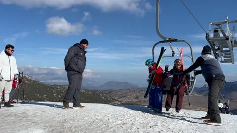 Staff helping two skiers get off the chairlift in davraz antalya ski resort Stock Footage 231699045