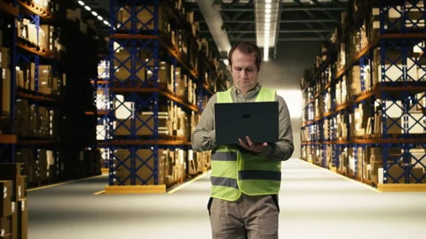 Staff member, using laptop for e-commerce, shipment details in warehouse Stock Footage 332908253