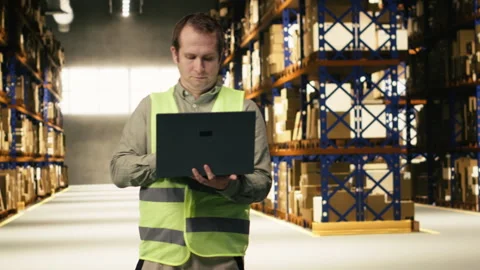 Staff member, using laptop for e-commerce, shipment details in warehouse Stock Footage 332910550