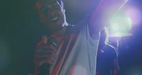 Stage cue flash, lead singer raising mic and singing, leaning and gesturing to Stock Footage 334111674