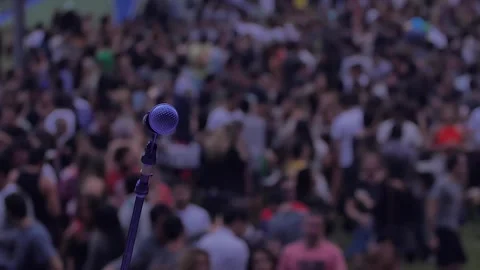 Stage microphone on focus while blurred crowd waits for concert on background 스톡 동영상 255680820