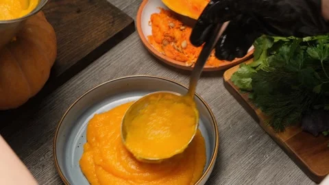 Stainless ladle smoothing hot pumpkin porridge in bowl with circular motion. Veg Stock Footage 332874997