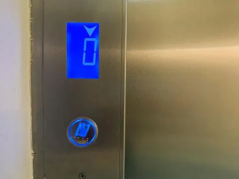 Stainless steel elevator panel with blue digital floor indicator showing ze.. Stockfoto's