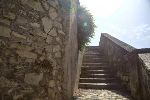 Staircase with balustrade next to a stone wall counter lit by the sun Stock Photos