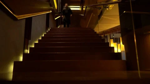 Stairs up to a dark bar with lights down comes a male waiter in black. He walks  Stock Footage 130132897