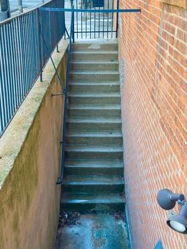 Stairs lead down from a brick wall to a concrete path in an urban setting d.. Stock Photos