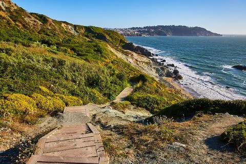 Stairs with no railing going down green hill toward rocky shore with small beach 스톡 사진