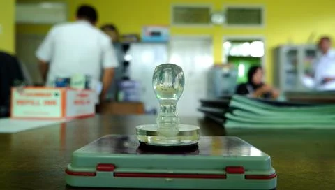 A Stamp That Is On The Table, With Office Employees In The Background Stock Photos