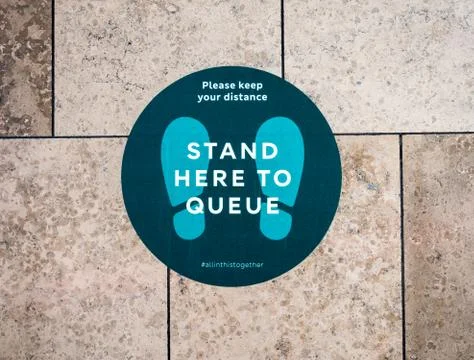 "Stand here to queue" floor sticker sign in shopping mall. Stock Photos