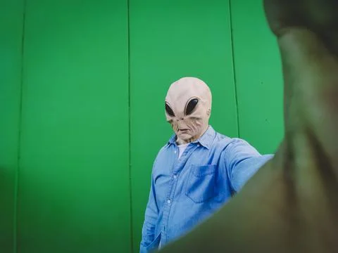 Standing alien mask face taking selfie picture against green background wall. Stock Photos