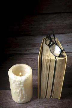 Standing book with reading glasses resting on top, next to a burning candle, Stock Photos