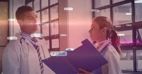 Standing doctors in lab coats, stethoscopes reviewing file in hospital hallway, Stock Photos