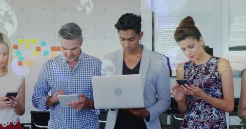 Standing five colleagues in workwear checking phones, tablet, laptop in office Stock Photos