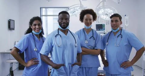 Standing group of four doctors in scrubs posing inside operating room, with s Stock Photos