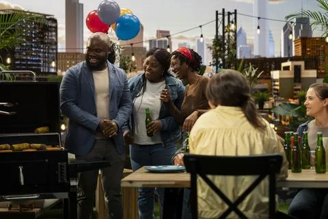 Standing group laughing and talking beside rooftop barbecue table and grill Stock Photos