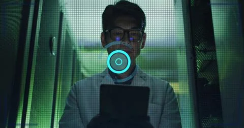 Standing Korean tech in white labcoat and glasses scanning data center server Stock Photos