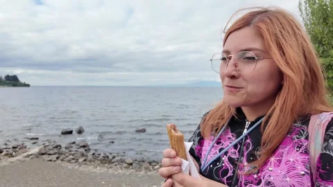 Standing by a Lake Holding a Snack on a Cloudy Day Stock Footage 313190684