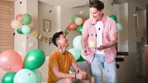 Standing man presenting cake for birthday, seated man taking it, confetti Stock Footage 334694218