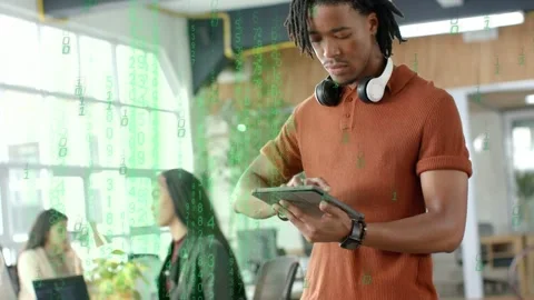 Standing man tapping tablet and initiating green code overlay in tech office, Stock Footage 333287590