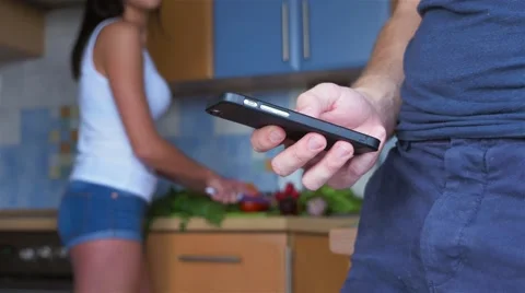 Standing man using mobile phone while woman peeling vegetables. Video stock 67502415