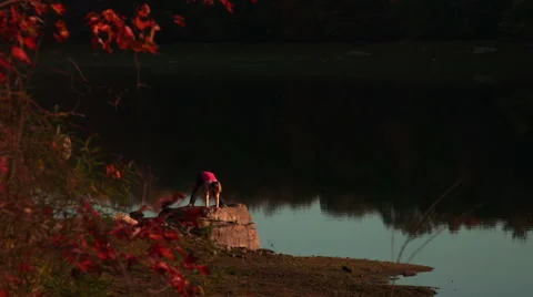 Standing straddle forward bend with twist on rock near lake Stock Footage 44120365
