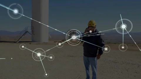 Standing tech in yellow hard hat, dark jacket holding phone near turbine, node Video stock 332469021