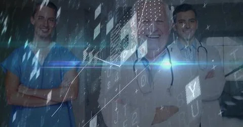 Standing three doctors in white coats and blue scrubs in clinic, stethoscopes Stock Photos