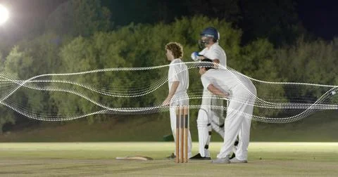 Standing three men in white cricket kit at night pitch, holding bat near stumps, Stock Photos
