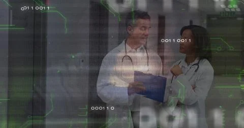 Standing two doctors consulting over blue clipboard in hospital corridor, with 库存照片