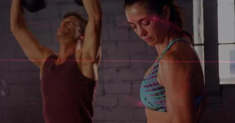 Standing woman patterned bra checking form loft gym man lifting kettlebells 写真素材