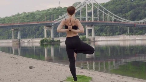 Standing yoga practicing. City beach and pedestrian bridge. River, lake. Stock Footage 112949953