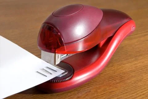 	Stapler of red color on a brown table. Stock Photos