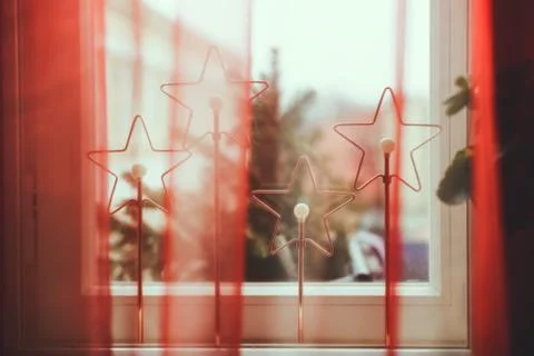 Star shaped lights in between window frames behind very sheer red curtain. Foto stock
