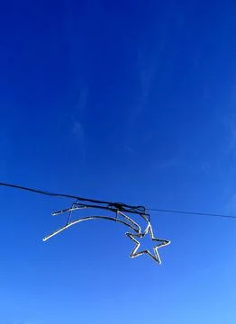 Star-shaped object hanging from an electrical wire against a vibrant blue sky Stock Photos
