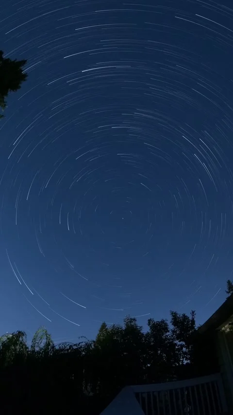 Starry Night Sky with Star Trails Over Silhouetted Landscape Stockbeeldmateriaal 348337364