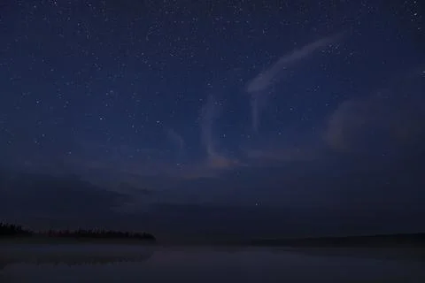 Starry night sky with wispy clouds over a tranquil lake Stock Photos