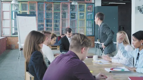 Start up team holds a meeting at a large table. Man manager gets up from a chair Stock Footage 108208333