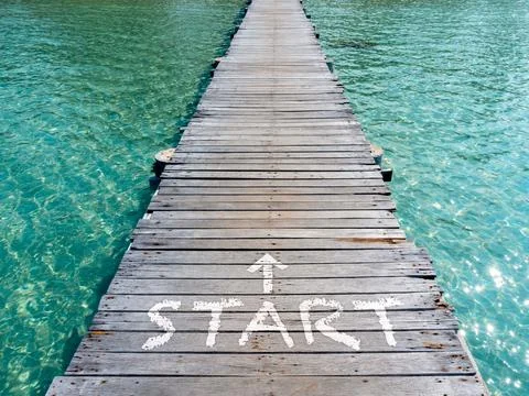 Start, white text and arrow on wooden bridge heading to the sea. Wood plank.. Foto stock