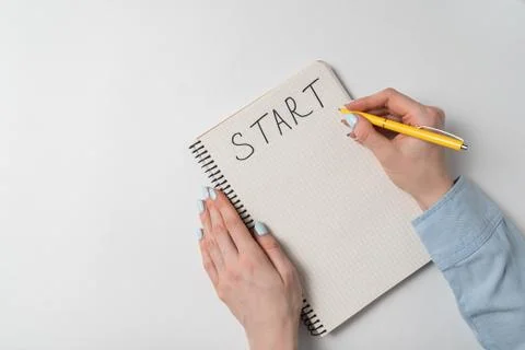 Start written on notebook over white background. Female hand writing in notep Фото