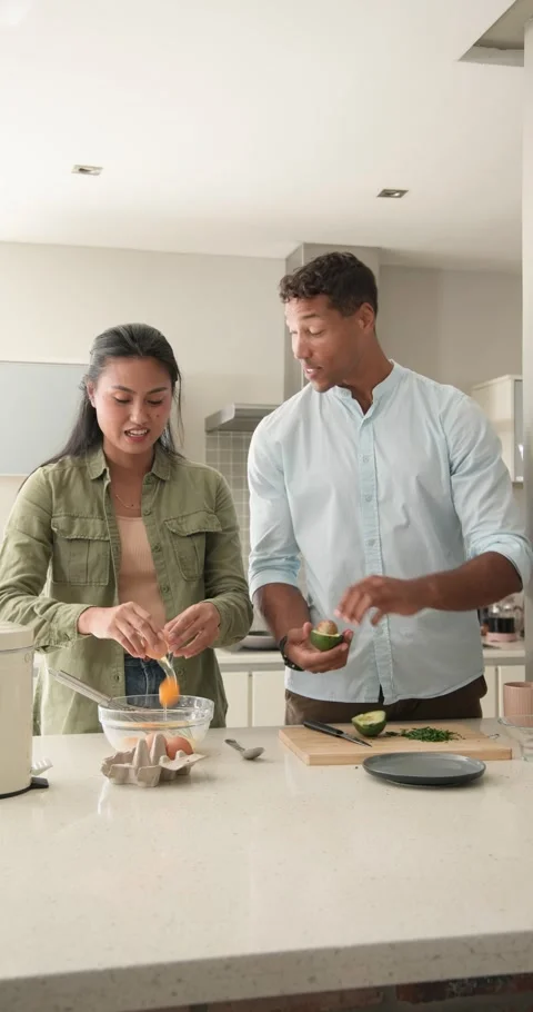 Starting by cracking eggs and slicing avocado, Diverse couple prepping meal at Stock Footage 345491071