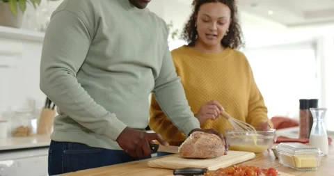 Starting meal prep, couple slicing roast on wooden cutting board, whisking eggs Stock Footage 342065567
