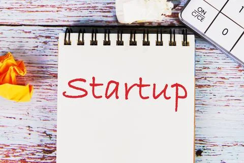 Startup word written on a sheet of notebook lying on old vintage boards wit.. Stock Photos